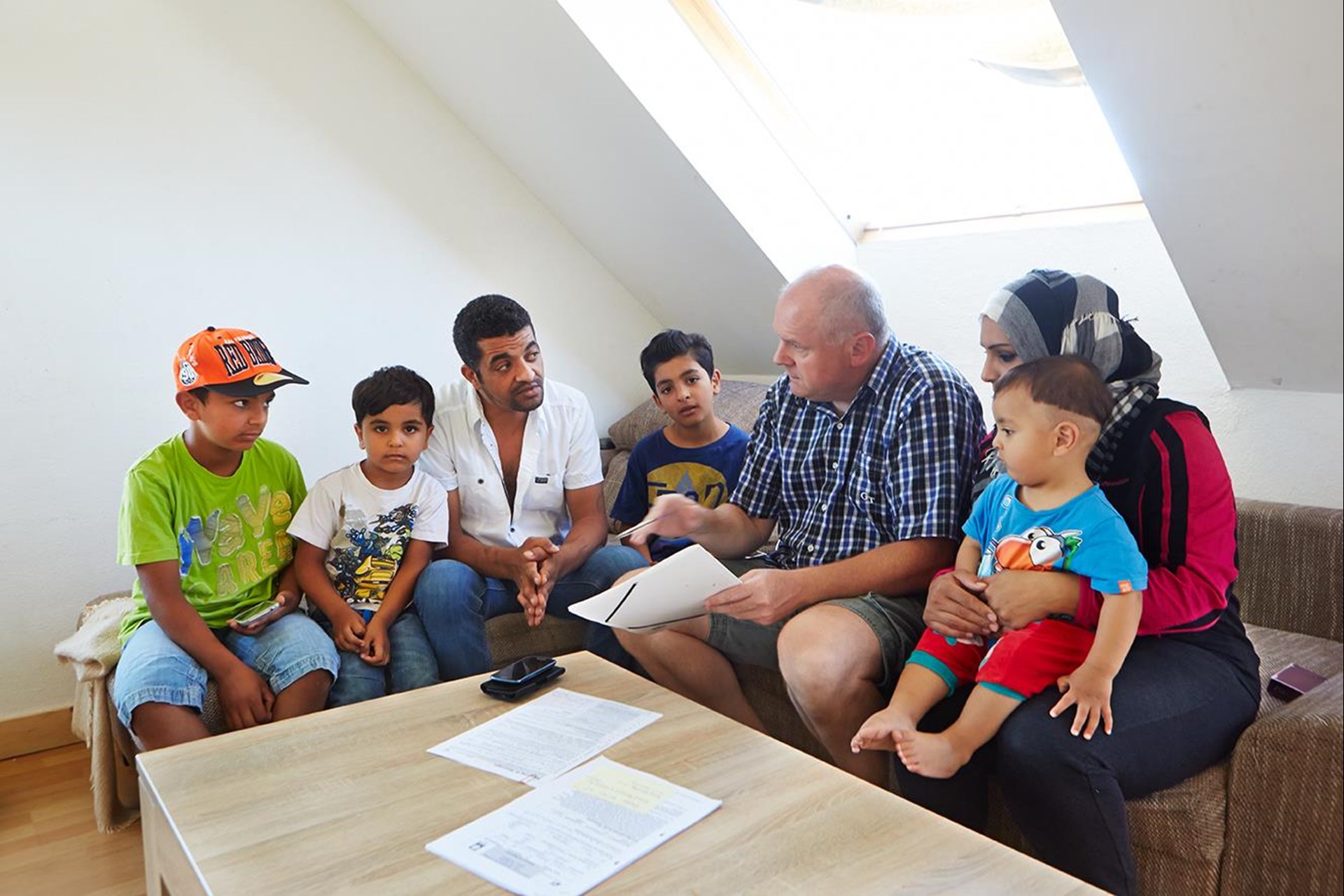Eine Familie sitzt mit einem anderen Mann am Tisch, vor ihnen Blätter.