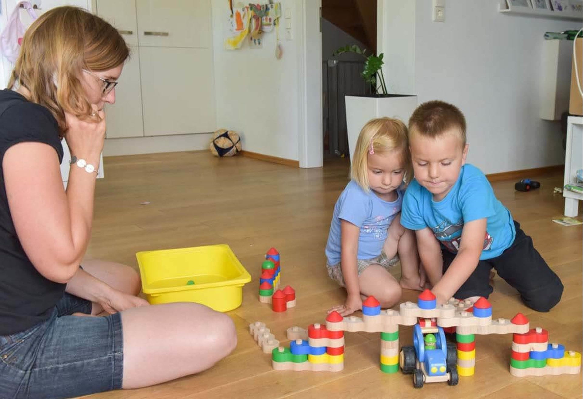 Kinder beim Spielen mit Spielzeug. Eine Erzieherin schaut zu.