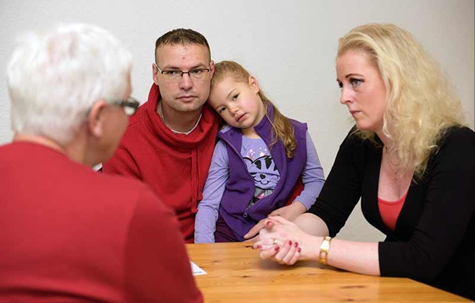Eine Beraterin sitzt am Tisch.
Ein Paar und ihr Kind sitzen auch am Tisch.
