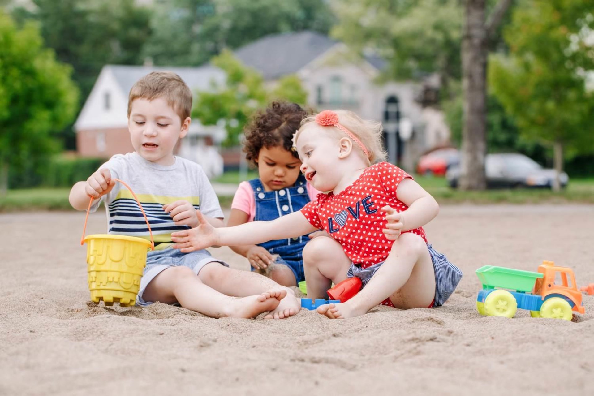 Drei kleine Kinder spielen zusammen im Sandkasten.